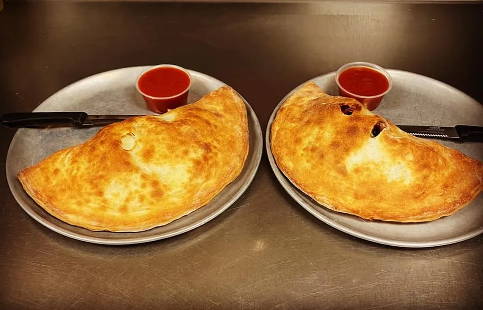 Two golden calzones with cups of marinara
