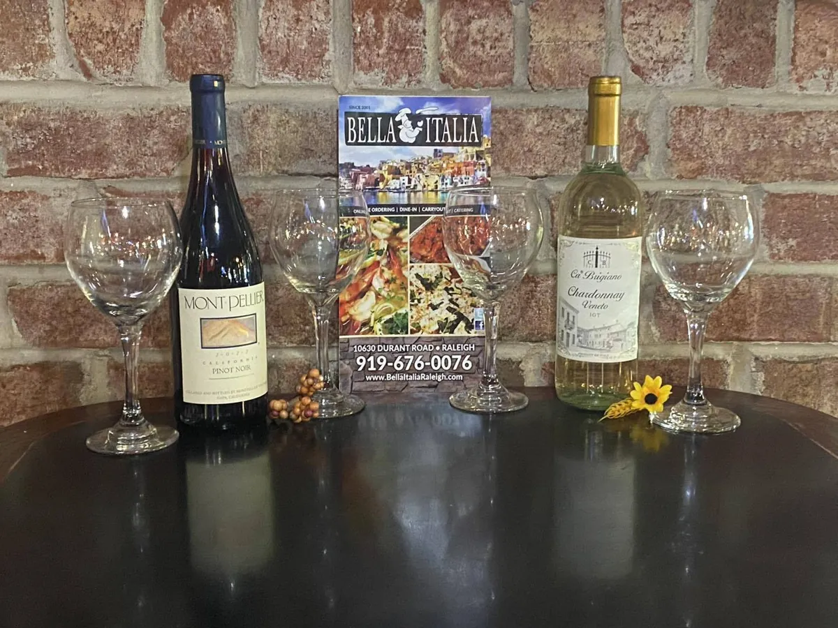 Bottles of red and white wine with glasses on a table in front of the restaurant's brick wall